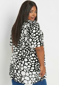 Blusa en blanco y negro con un patrón similar a burbujas, mangas cortas y un ajuste relajado, con un dobladillo curvado y textura suave.