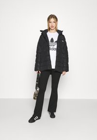Crna puffer jakna s teksturiranim završetkom, s visokim ovratnikom. Uparena s bijelim T-shirtom s Adidas logotipom i crnim flared hlačama, uz torbu sa životinjskim uzorkom.