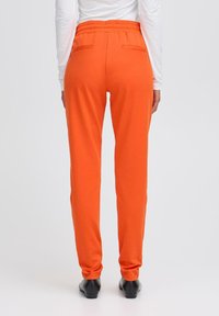 Oranje joggerpants van zachte stof, met een elastische tailleband en twee achterzakken. Tapered leg ontwerp met een gladde textuur.