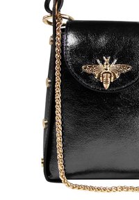 Sac en cuir verni noir avec un embellissement en forme d'abeille dorée, une bandoulière en chaîne et des accessoires décoratifs dorés sur les côtés.