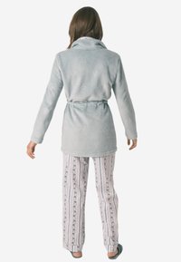Accappatoio in pile azzurro chiaro con colletto sciallato e cintura in vita, abbinato a pantaloni da pigiama a righe con motivi floreali in colori pastello.