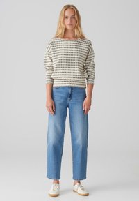 Lightweight striped sweater in beige and dark green, featuring a wide neckline and three-quarter sleeves, paired with relaxed-fit blue jeans.