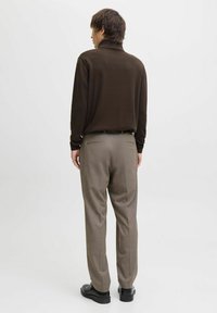 Brown long-sleeve polo with a high collar, paired with tailored light brown trousers and black shoes. Smooth textures, subtle detailing.