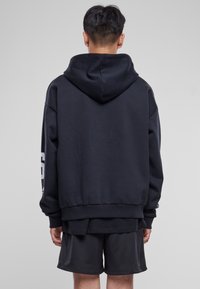 Sudadera con capucha negra de corte relajado, hecha de una tela suave, con un bolsillo tipo canguro y una gran impresión en la manga izquierda.