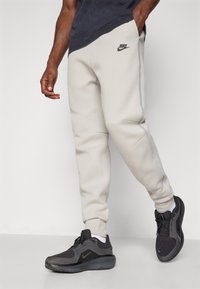 Ljusgrå Nike-joggers med åtsittande mudd, sidofickor och en liten svart logotyp. Matchas med svarta sportskor med texturerad ovandel.