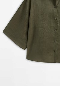 Chemise boutonnée vert olive avec manches larges jusqu'au coude et tissu texturé visible.