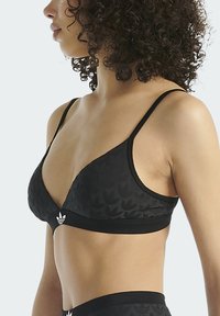 Zwarte triangular bralette met een getextureerd bloemmotief, dunne verstelbare bandjes en een logo-accent op het midden van de onderband.
