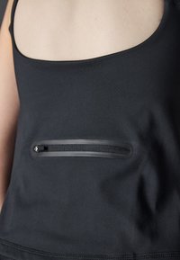 Svart atletisk tank topp med scoop-hals og glidelås lomme detaljer. Jevn tekstur, tettsittende design, minimale sømakkenter.