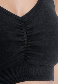 Zwarte sportbeha met een diepe V-hals, geplooide textuur in het midden en een geribbelde tailleband voor extra ondersteuning.