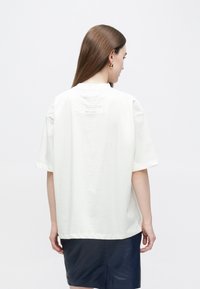 Biele bavlnené tričko s krátkymi rukávmi, okrúhlym výstrihom a vyšitým logom na chrbte. Hladká textúra a pohodlný strih.