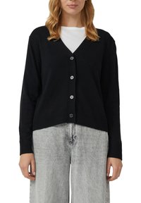 Czarny kardigan z dekoltem w serek, zapinany na guziki z przodu, z prążkowanym dołem. Wykonany z miękkiego materiału, zestawiony z jasnoszarymi szerokimi spodniami.