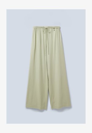 Pantalones de pierna ancha en verde claro con cintura elástica, cordón ajustable y un sutil logotipo en el lateral. Textura suave y corte relajado.
