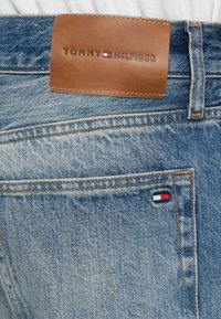Blue denim jeans with a brown leather label and Tommy Hilfiger logo above the back pocket.