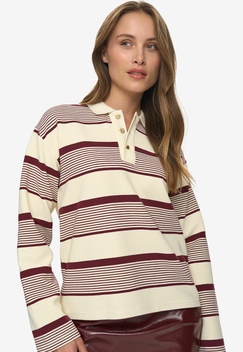 Polo a maniche lunghe a righe color bordeaux e crema con colletto e tre bottoni. Presenta una texture a costine e orlo dritto.
