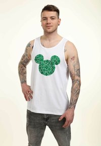 Top de tirantes blanco con un gráfico de Mickey Mouse en estilo mosaico en verde en el pecho. El modelo tiene tatuajes y lleva puestos unos jeans grises.