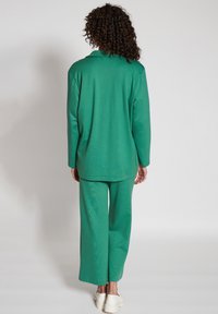 Grön långärmad topp med en löst sittande passform och rund halsringning, matchad med breda byxor i samma tyg, tillverkade av mjukt, texturerat material.