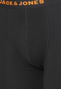 Schwarze Baumwollslips mit einem elastischen Bund, der "JACK & JONES" in orangefarbener Schrift zeigt. Glatte Textur mit kontrastierenden Nähten.