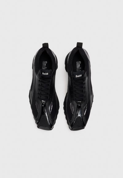 Zapatillas deportivas negras con parte superior de malla, acentos brillantes y paneles texturizados. Presenta un diseño con cordones y una suela acolchada.