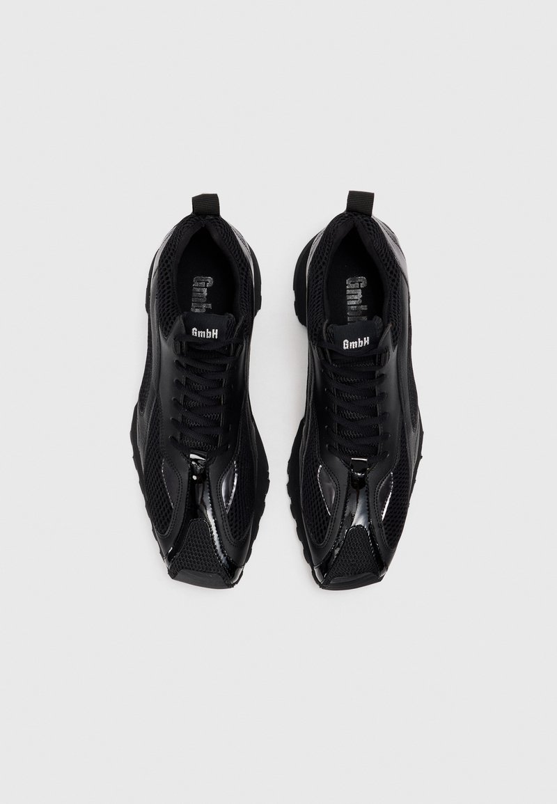 Sorte atletiske sko med en overdel i mesh, glansfulde accenter og teksturerede paneler. Har et snørebåndsdesign og en polstret sål.
