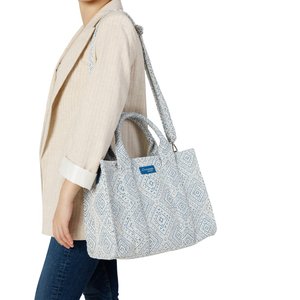 Persona con blazer beige y vaqueros, llevando un bolso tote grande con patrón azul y blanco, con asas dobles y correa para el hombro.