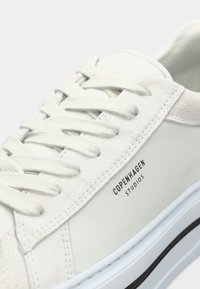 Weißer Sneaker mit Wildleder- und glatten Ledertexturen, ausgestattet mit hellfarbenen Schnürsenkeln, einem Logo mit der Aufschrift "COPENHAGEN STUDIOS" und einer weißen Sohle mit schwarzem Rand.