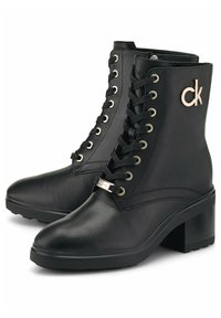 Botas de tobillo de cuero negro con punta redonda, cierre de cordones en la parte delantera, ojales dorados y un logo dorado de CK en el lado. Tacón ancho y acabado texturizado.