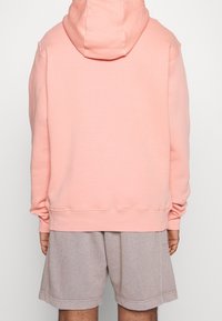 Persikofärgad hoodie med långa ärmar och ribbade muddar, ihop med grå spräckliga shorts. Enkelt, avslappnat design.