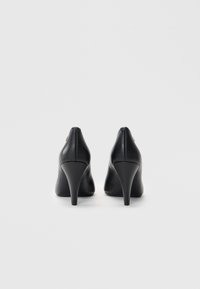 Sorte læder højhælede sko med spids tå og en glat overflade. Har en slank hæl og subtile metalliske detaljer bagpå.