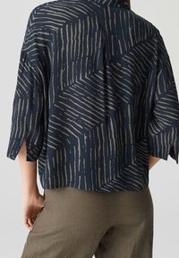 Blusa blu navy con un motivo a zigzag testurizzato in beige chiaro, con maniche larghe e una vestibilità rilassata. Il tessuto è leggero e morbido.