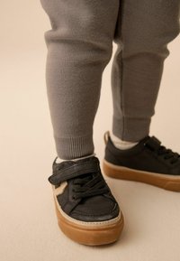 Svarta lädersneakers med en beige gummisula, utrustade med en kardborrerem och snören. Grå stickade leggings med ribbade manschetter.
