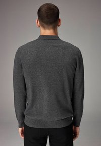 Suéter gris de punto con mangas largas, dobladillo y cuello acanalados, que presenta una textura suave y una silueta ajustada. Se lleva con pantalones oscuros.
