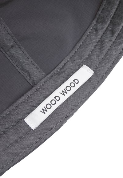 Sivi materijal s bijelom pravokutnom etiketom ušivenom, koja prikazuje naziv branda "WOOD WOOD" u crnim velikim slovima.