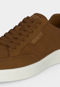 Baskets Guess marron avec motif de logo embossé, lacets marron assortis et semelle blanche.