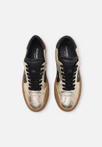 Metallic gold leather sneakers feature black laces, black accents, and a gum rubber sole, with a textured finish and padded collar.