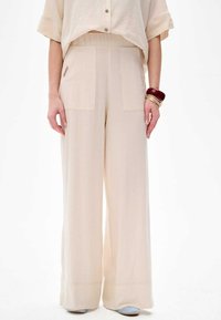 Beige weite Hose mit hoher Taille, aus leichtem Stoff. Verfügt über aufgesetzte Taschen vorne und eine glatte, fließende Textur.