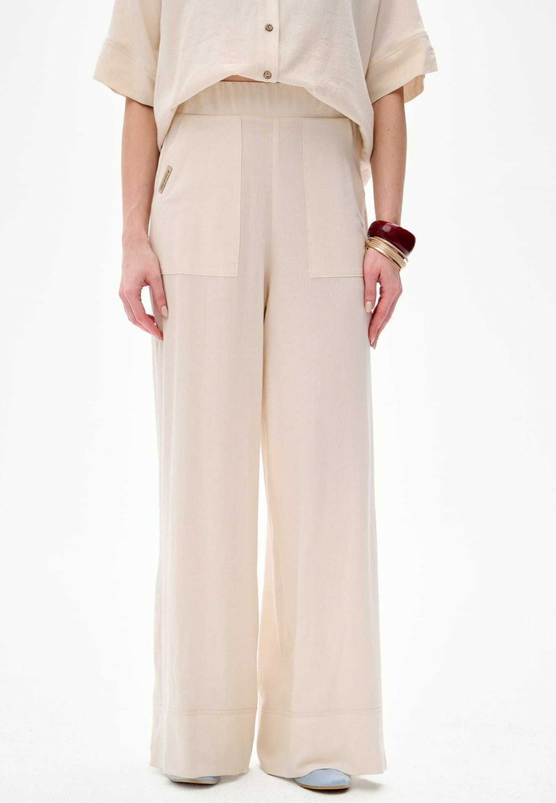 Beige weite Hose mit hoher Taille, aus leichtem Stoff. Verfügt über aufgesetzte Taschen vorne und eine glatte, fließende Textur.