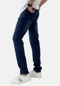 Vaqueros azules de corte recto, hechos de mezclilla. Con un diseño clásico de cinco bolsillos y combinados con zapatillas blancas con acentos negros.