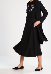 Musta hame, jossa on lievä liehuke, yhdistetty mustaan kirjailtuun kukkatoppiin ja pitkään mustaan takkiin. Päällä mustat ballerinat, sileäpintaiset.