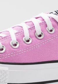 Ljust rosa canvas sneakers med vita snören, silverfärgade ögla och en texturerad gummisula. Har svart logotyp på tungan.