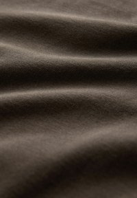 Smeđa tkanina glatke teksture, s diskretnim valovima i finim tkanjem. Materijal izgleda mekan i savitljiv.