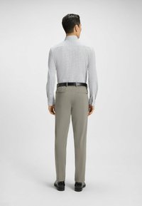 Męska koszula z długim rękawem w jasny wzór, zestawiona z beżowymi spodniami. Koszula ma kołnierzyk i dopasowany krój, podczas gdy spodnie mają klasyczny fason.