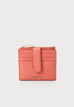 Coral leather wallet with textured surface, zip closure, multiple card slots, and a magnetic flap. Features gold branding at the front.