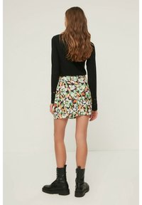 Mini-jupe florale sur fond noir avec des fleurs vertes, oranges et blanches. Assortie à un haut noir à manches longues et des bottes de combat noires.