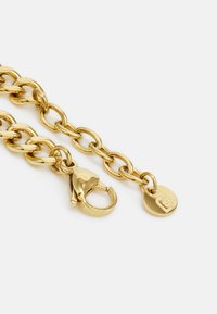 Gold chain featuring thick, interlinked oval links. Includes a lobster clasp and a circular tag with a logo detail. Smooth, shiny finish.