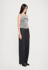 Γκρίζα ριγέ αμάνικη μπλούζα με κείμενο "Moschino Jeans", συνδυασμένη με ψηλόμεσα, φαρδιά τζιν παντελόνια σε σκούρο χρώμα. Το μοντέλο φοράει μαύρα τακούνια.