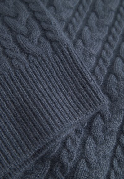 Tmavě modrý pletený svetr s kabelkovým vzorem a žebrovanými manžetami, vyrobený z měkké vlny, zdůrazňující texturu a pečlivé řemeslné zpracování.