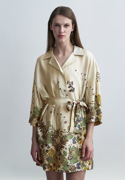Robe courte en soie présentant un imprimé floral intégral aux tons terreux, avec un devant boutonné et une taille ceinturée. Manches trois-quarts.