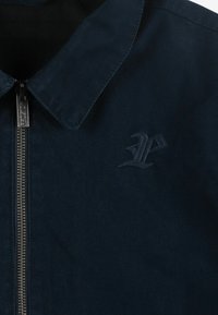 Ciemnoniebieska kurtka z kołnierzem, przednim zamkiem i haftowanym logo, charakteryzująca się teksturowanym materiałem oraz prostym, minimalistycznym designem.