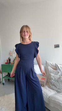 Mørkeblå jumpsuit med korte volangermer, skreddersydd bodice, vid ben-design og plisserte detaljer foran. Glatt stoff med minimal detaljering.