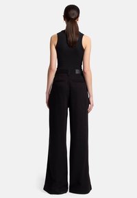 Pantalons noirs évasés en tissu lisse, taille haute, et deux poches au dos. Le haut est un débardeur noir ajusté.